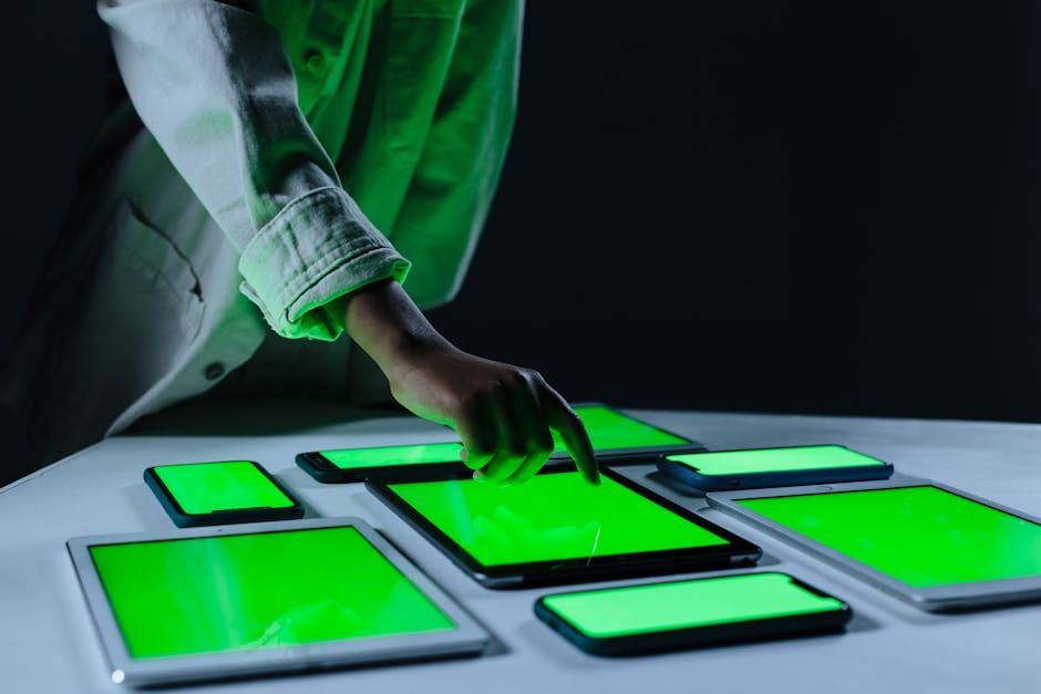 Hand interacting with multiple digital tablets on a green screen setup indoors
